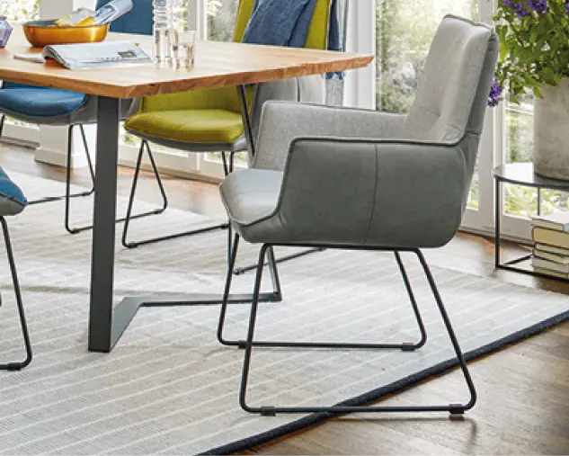 Gepolsterter Esszimmerstuhl mit Armlehnen in Grautönen, schlankes Metallgestell, stilvolle Sitzlösung für moderne Esszimmer mit Holztisch, Teppich und bodentiefen Fenstern